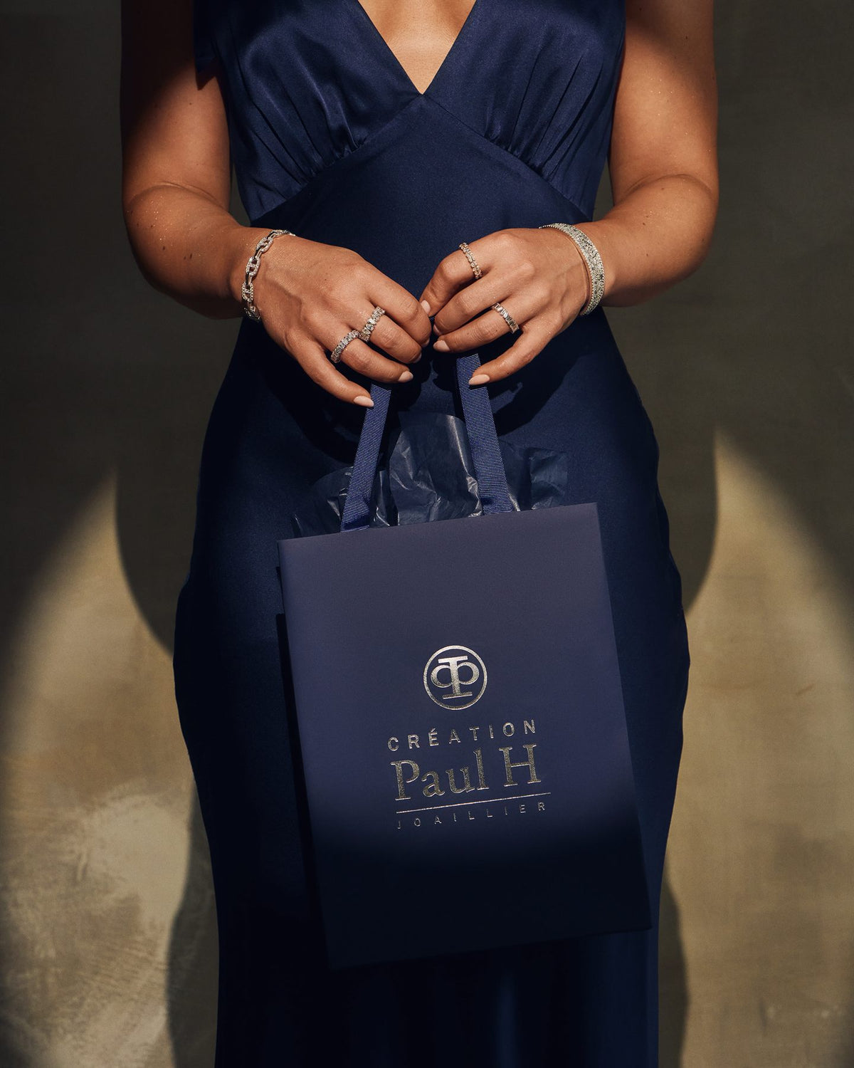 A navy Creation Paul H gift bag held in hand, diamond rings and bracelets catching the light