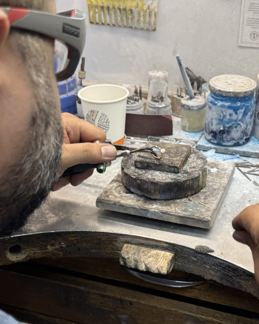 A jeweler at the bench, working a diamond ring with tweezers above the soldering block