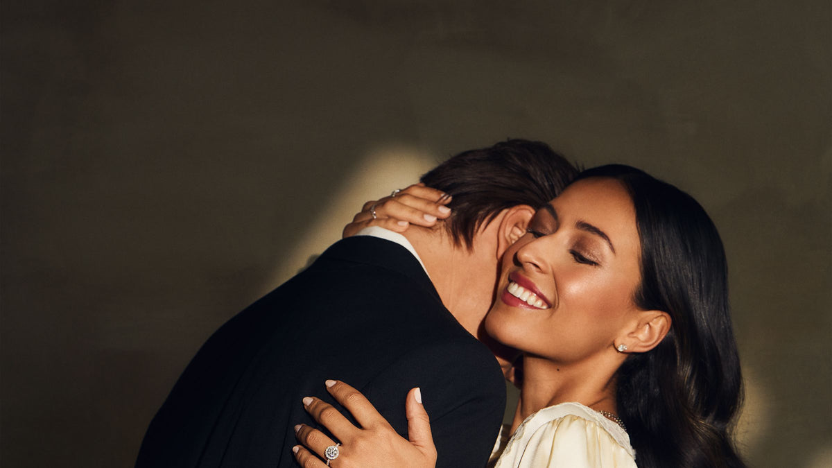Couple embracing, she wears a halo engagement ring and tennis bracelet