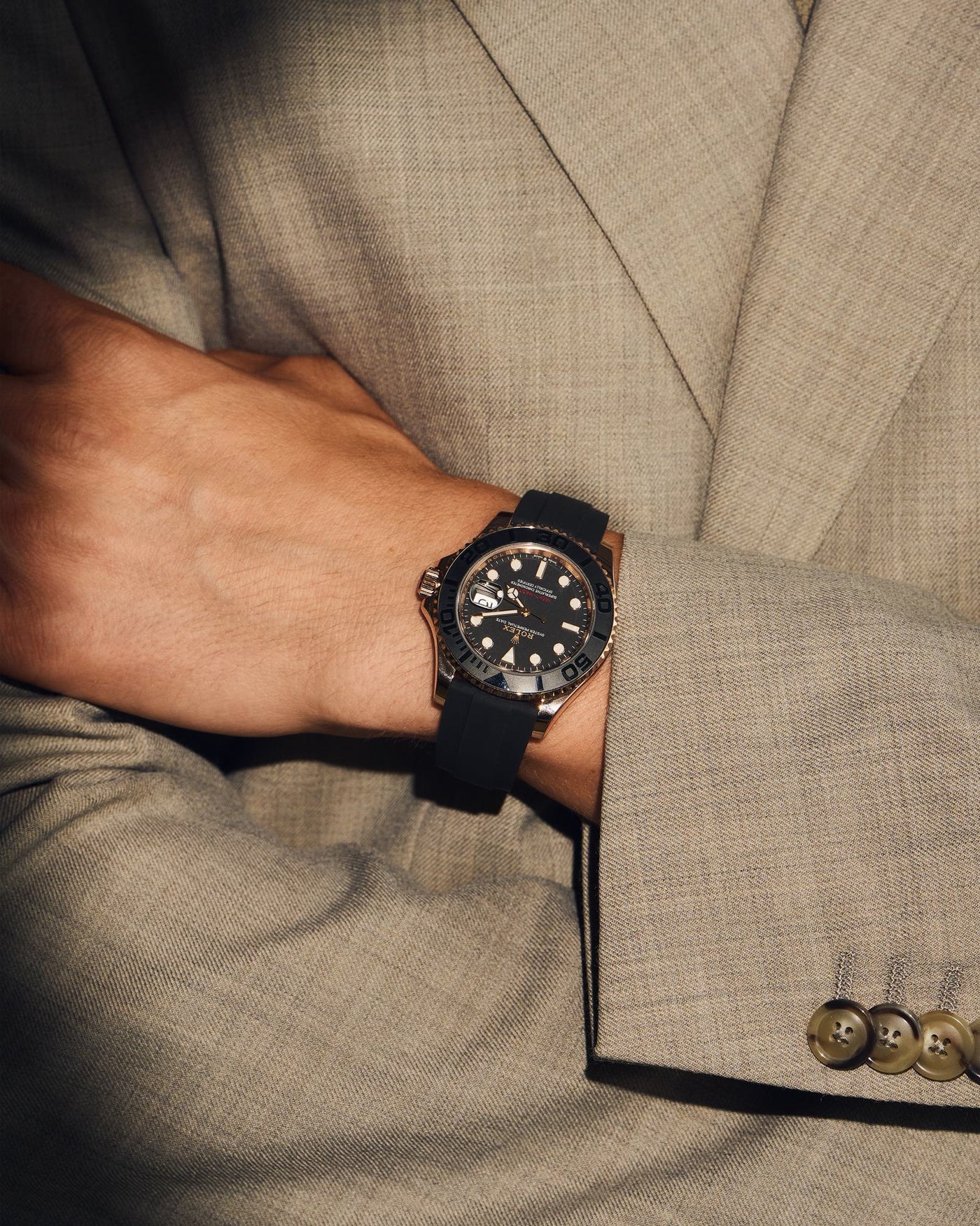 Rose gold watch on a crossed wrist, taupe suit