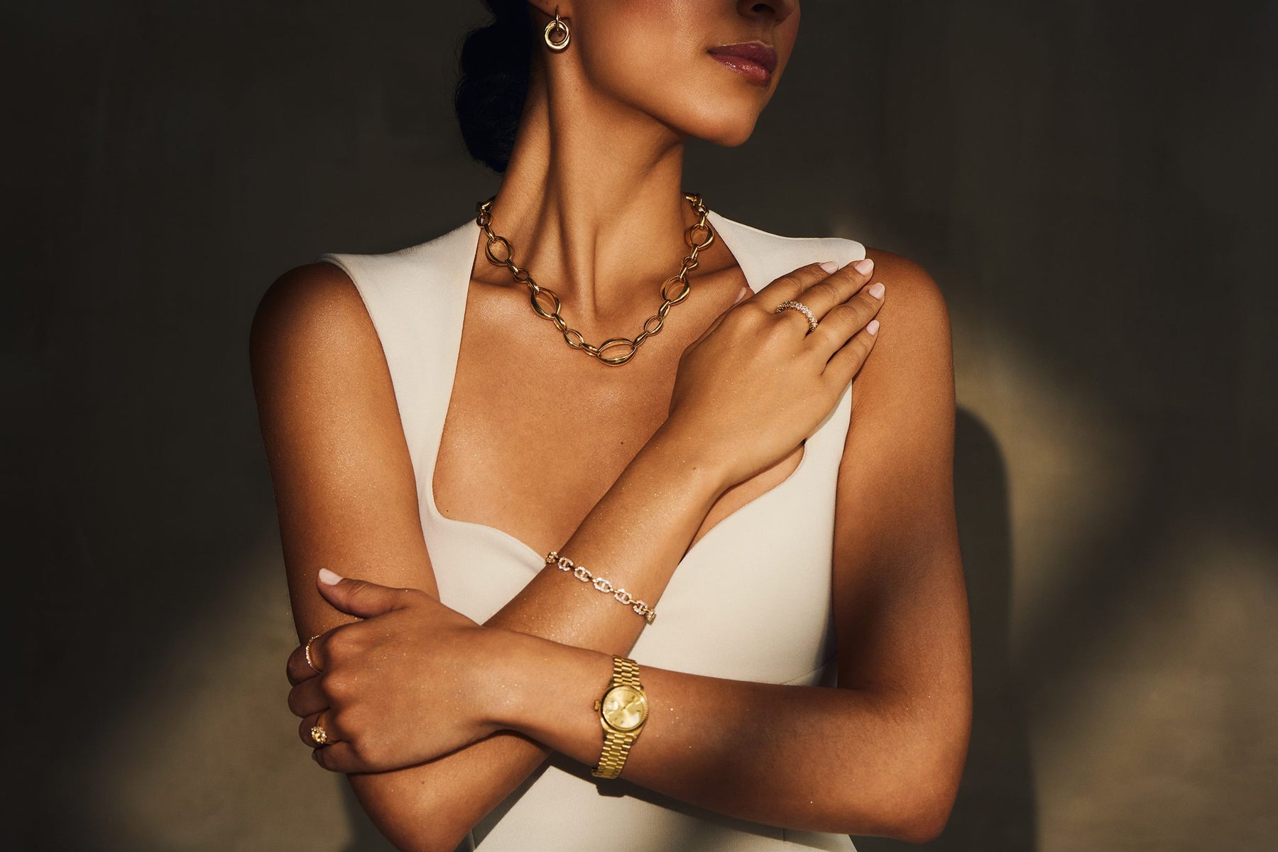 Gold link necklace, diamond bracelet and gold watch worn with a white dress, editorial portrait