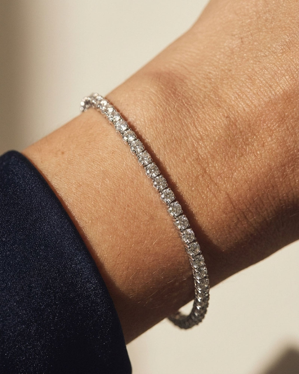Diamond tennis bracelet worn on the wrist with navy silk sleeves, warm editorial light. Representative made-to-order image