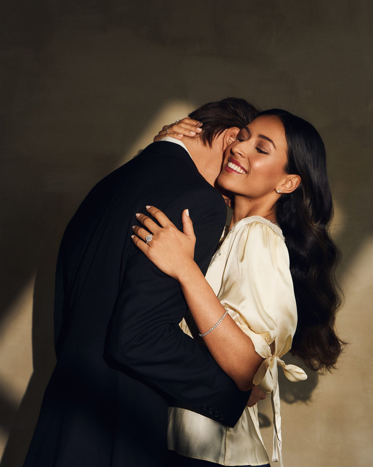 A couple embracing, her engagement ring and bracelet in the light